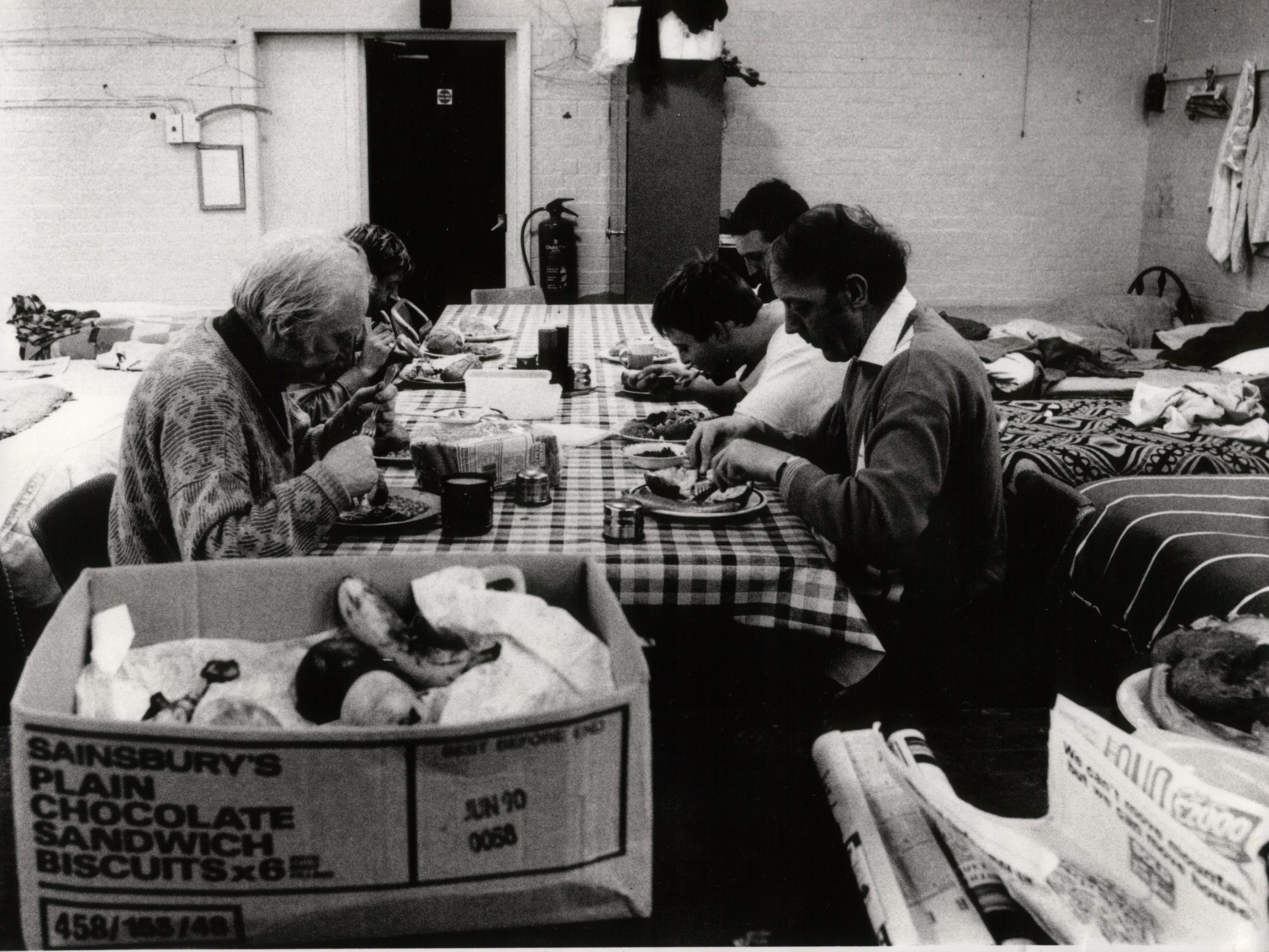 SSJ our history image. SSJ Our history image. Few homeless people sitting around a table eating, when The Society of St James was first established.